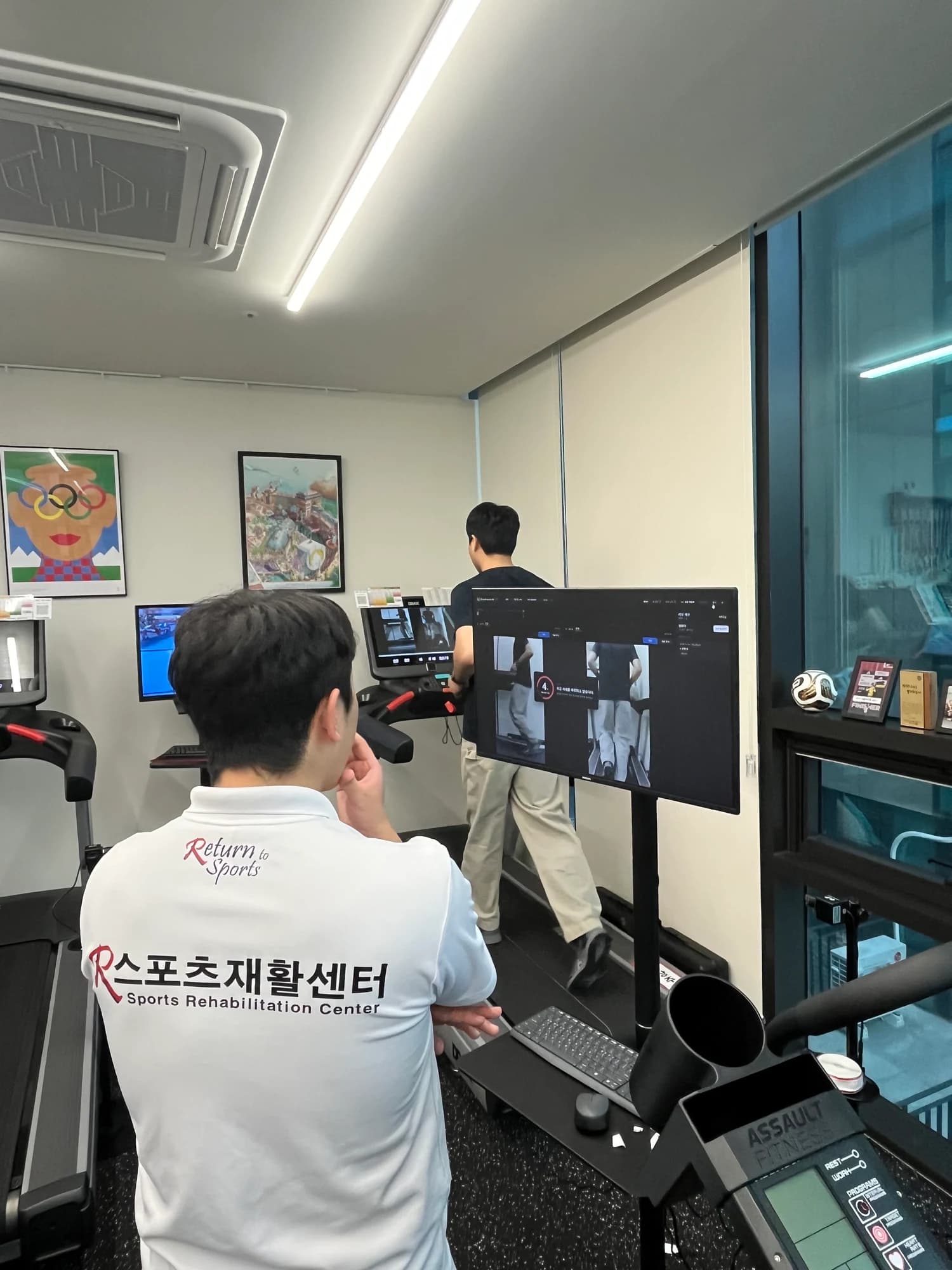 A coach watches a treadmill runner and the recording monitor